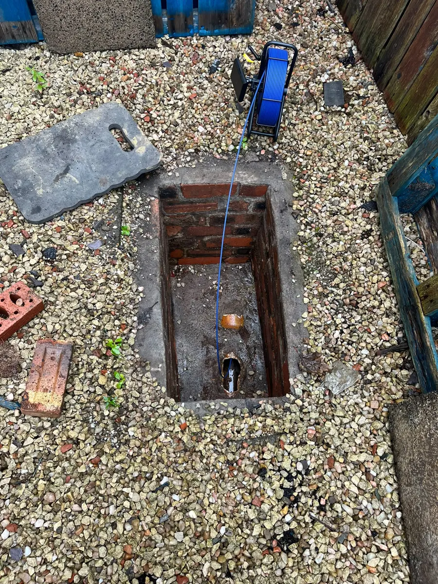 Open drain chamber in a gravel garden with the CCTV camera cable going in