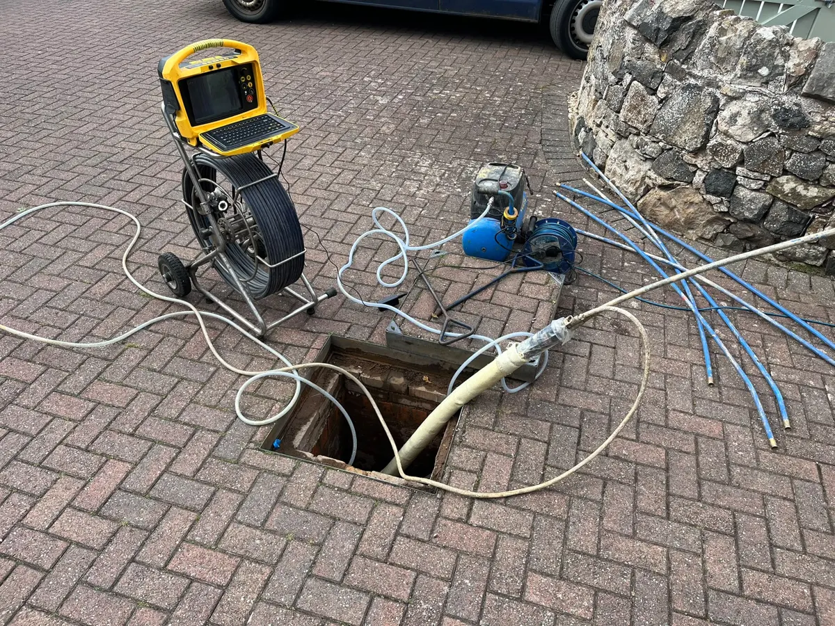 CCTV survey reel and jetting hose set up at an open manhole on a block-paved driveway