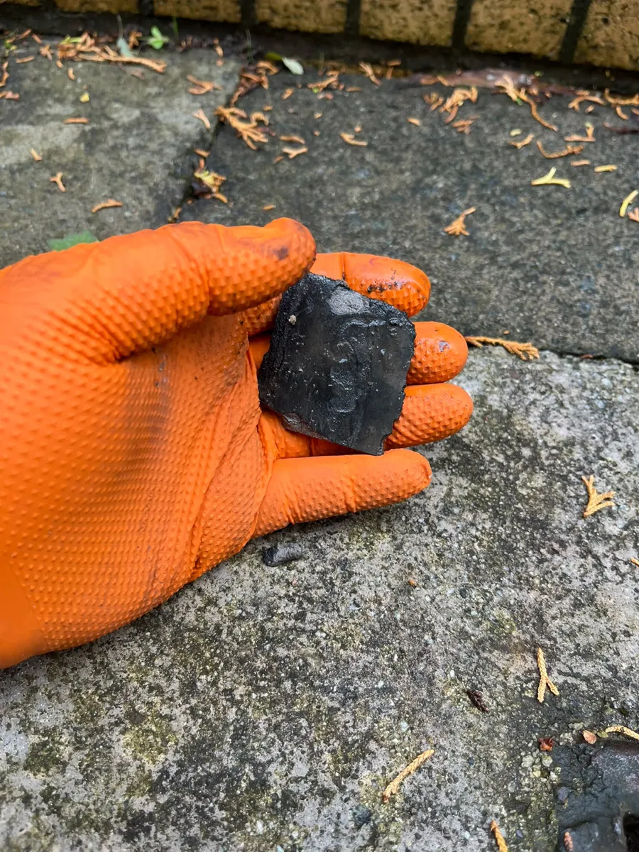 Gloved hand holding a lump of hardened debris pulled from a blocked drain